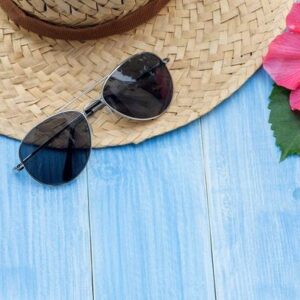 hat, sunglasses, sunblock and chinese rose flower on a blue wooden table.