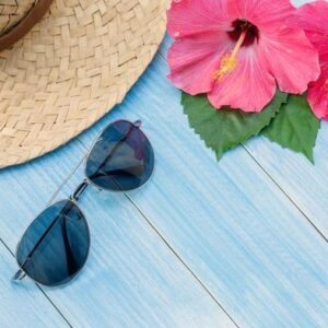 hat, sunglasses, sunblock and chinese rose flower on a blue wooden table.