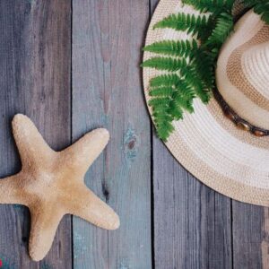 a hat, a fern leaf, a starfish, sea shells on the wooden background