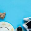 travel accessories camera, straw hat, card, shoes on a blue background flat top view layout with copy space