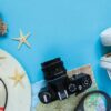 travel accessories camera, straw hat, card, shoes on a blue background flat top view layout with copy space