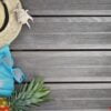 top view on straw hat, beach towel, sunglasses and pineapple on wooden terrace