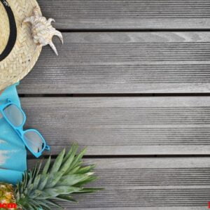 top view on straw hat, beach towel, sunglasses and pineapple on wooden terrace