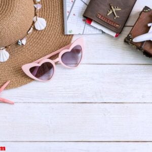 beach hat with travel items on white wooden background, summer vacation concept