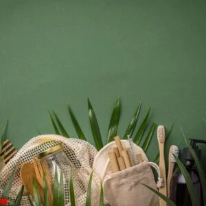 zero waste concept. cotton bag, bamboo cultery, glass jar, bamboo toothbrushes, hairbrush and straws on green background