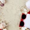 christmas hat and red sunglasses on the beach. santa hat and eyeglasses on the sand near shells. holiday. new year vacation. copy space. frame. top view.