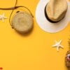 colorful summer female fashion outfit flat lay. straw hat, bamboo bag, pineapple in sunglasses and starfish over yellow background, top view. summer fashion, holiday concept.