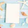 blank notebook and seashells on blue wooden floor.