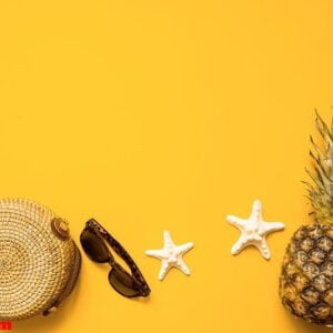 colorful summer female fashion outfit flat lay. bamboo bag, sunglasses, pineapple and starfish over yellow background, top view. summer fashion, holiday concept