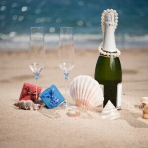 bottle of champagne on the beach with a gift boxes and shells