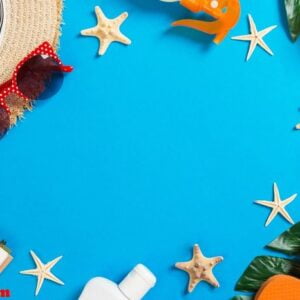 beach accessories with straw hat, sunscreen bottle and seastar on blue background top view with copy space