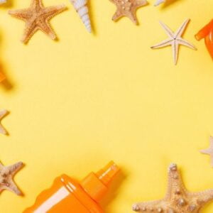 sunscreen cream with starfish and seashells in bottles on yellow background, top view