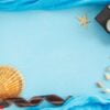 blank paper photo frame with starfish, shells and items on wooden table.