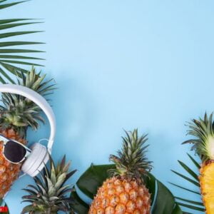 funny pineapple wearing white headphone, concept of listening music, isolated on colored background with tropical palm leaves, top view, flat lay design.