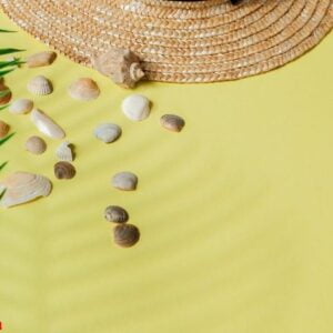 summer holiday background. tropical summer concept with woman fashion accessories, leaves and seashells on yellow background. flat lay, top view