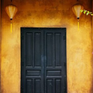 a beautiful black wooden door on a yellow wall with chinese lanterns. vietnam.