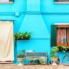 blue aqua colored house with flowers, bench and a bicycle. colorful houses in burano island near venice, italy.