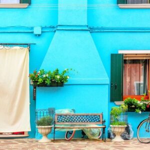 blue aqua colored house with flowers, bench and a bicycle. colorful houses in burano island near venice, italy.