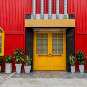 a bright red building with a yellow door and window, flower pots with plants against a red metal wall on a city street in vietnam