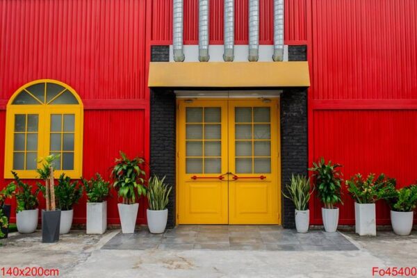 a bright red building with a yellow door and window, flower pots with plants against a red metal wall on a city street in vietnam