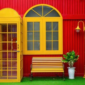 a bright yellow telephone box and flower pots with plants, a bench and a lamp post against a red metal wall on a street in da nang, vietnam