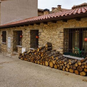 firewood stacked on the facade of an old house made of stone and bicycle parked at the entrance.