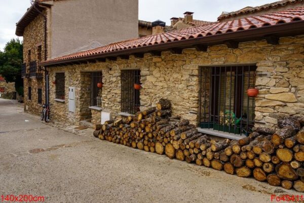 firewood stacked on the facade of an old house made of stone and bicycle parked at the entrance.