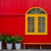 a large yellow window, flower pots with plants and a bench against a red metal wall on a city street .