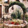 old wooden stone well with red flower arch and ivy in perouges, france