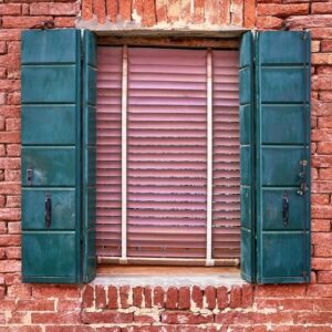 window with green shutters on red brick wall of houses. italy, venice, burano.