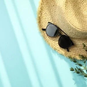 straw hat, branch and sunglasses on blue background