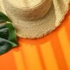 straw hat and palm leaf on orange background