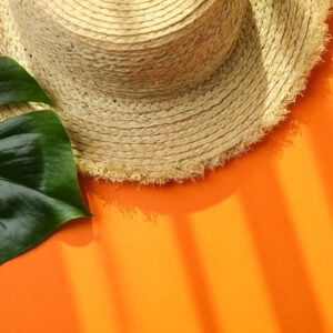 straw hat and palm leaf on orange background