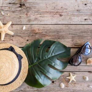 beach accessories: glasses and hat with shells and sea stars on a colored background