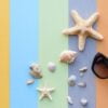 beach accessories: glasses and hat with shells and sea stars on a colored background