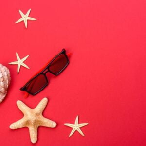 beach accessories: glasses and hat with shells and sea stars on a colored background