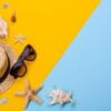 beach accessories: glasses and hat with shells and sea stars on a colored background