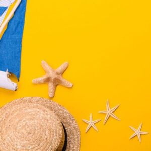 beach accessories: glasses and hat with shells and sea stars on a colored background