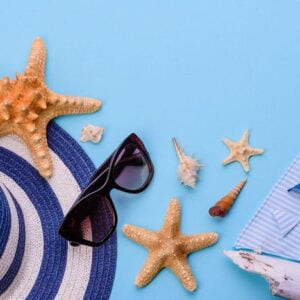 beach accessories: glasses and hat with shells and sea stars on a colored background