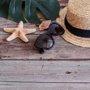 beach accessories: glasses and hat with shells and sea stars on a colored background