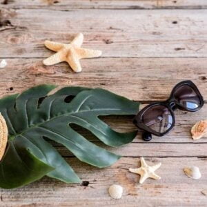 beach accessories: glasses and hat with shells and sea stars on a colored background