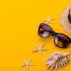 beach accessories: glasses and hat with shells and sea stars on a colored background