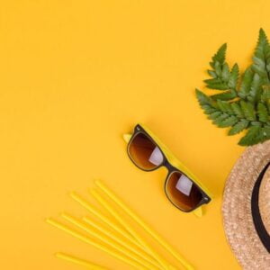 beach accessories: glasses and hat with shells and sea stars on a colored background