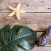 beach accessories: glasses and hat with shells and sea stars on a colored background