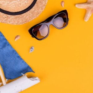 beach accessories: glasses and hat with shells and sea stars on a colored background