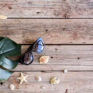 beach accessories: glasses and hat with shells and sea stars on a colored background