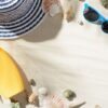 beach hat, sunglasses, and sunscreen are among the seashells on the sand