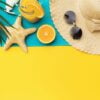 beach holiday accessories, orange juice and palm leaf on a yello