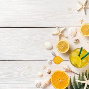 citrus fruits, iced cocktail, seashells and starfish on a white wooden background.