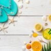 colorful summer background. cocktail with ice, oranges, lemons, shells, starfish and flip flops on a light wooden background.